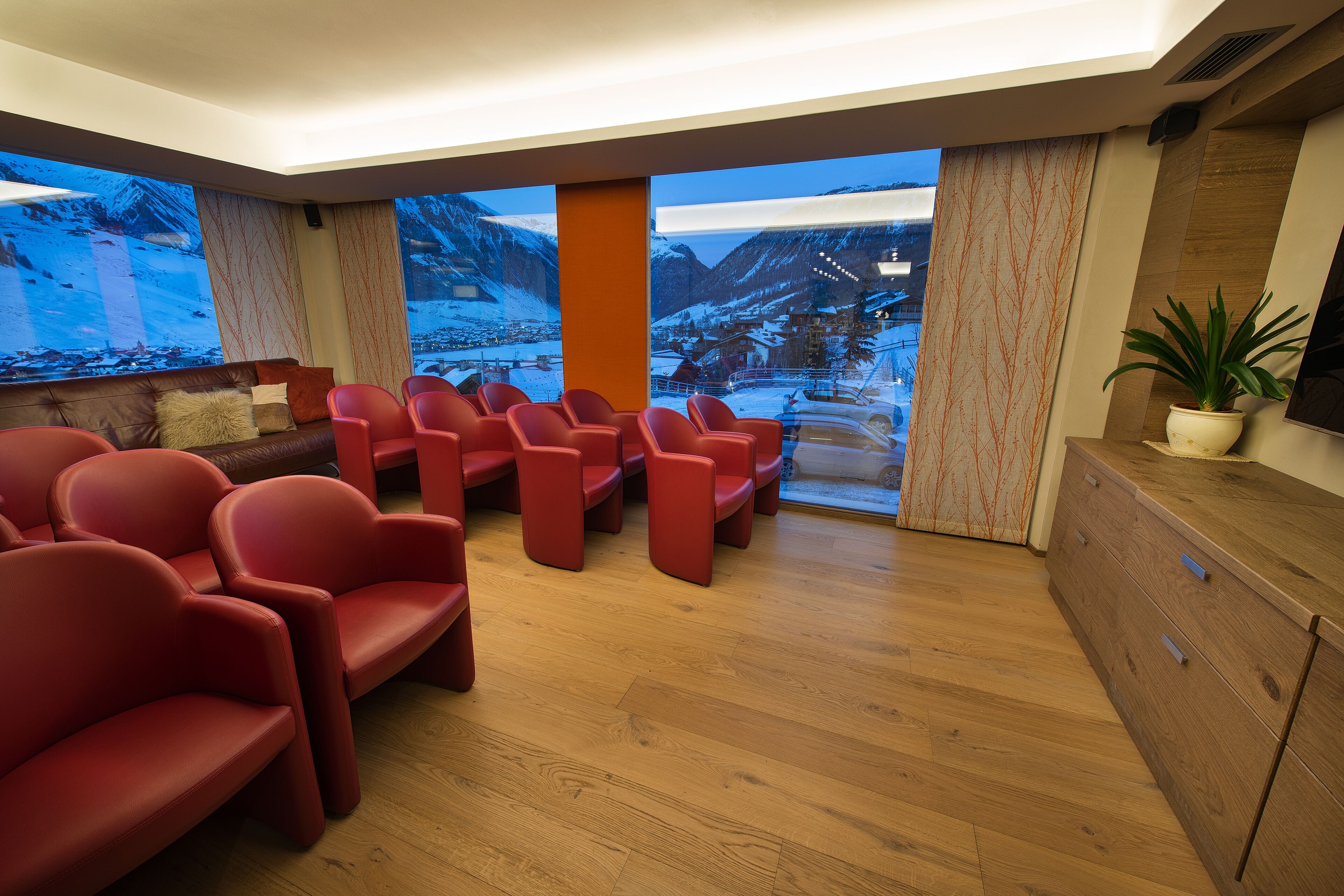 A modern lounge area with red seating, wooden flooring, and large windows offering a snowy mountain view.