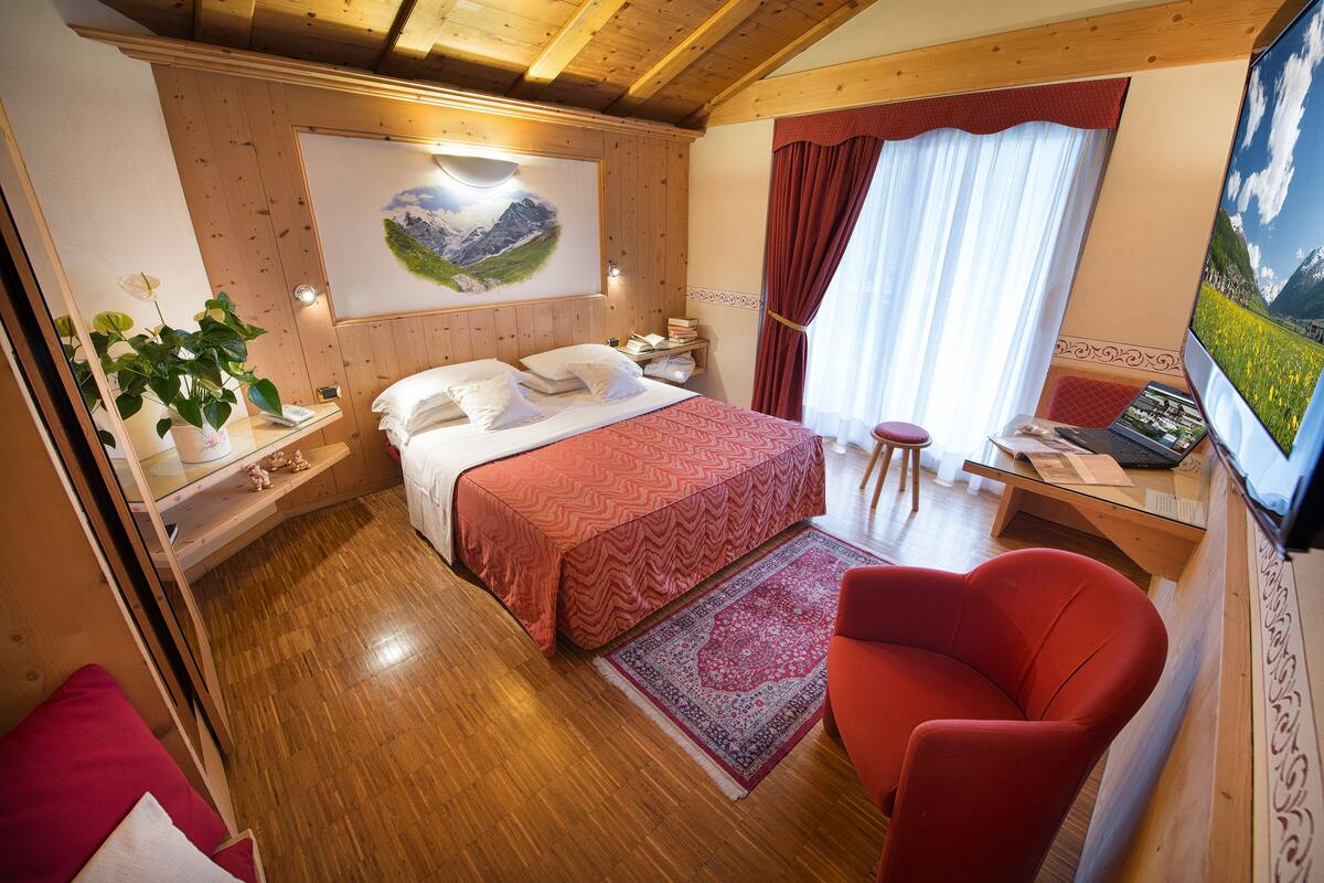 Una habitación acogedora con cama, escritorio, silla y un amplio ventanal con cortinas.