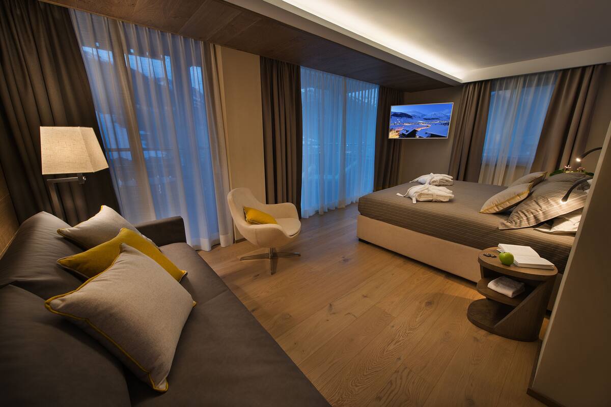 Una habitación de hotel moderna con una cama grande, un sofá, una silla, un televisor y una mesita con una lámpara y una manzana verde.