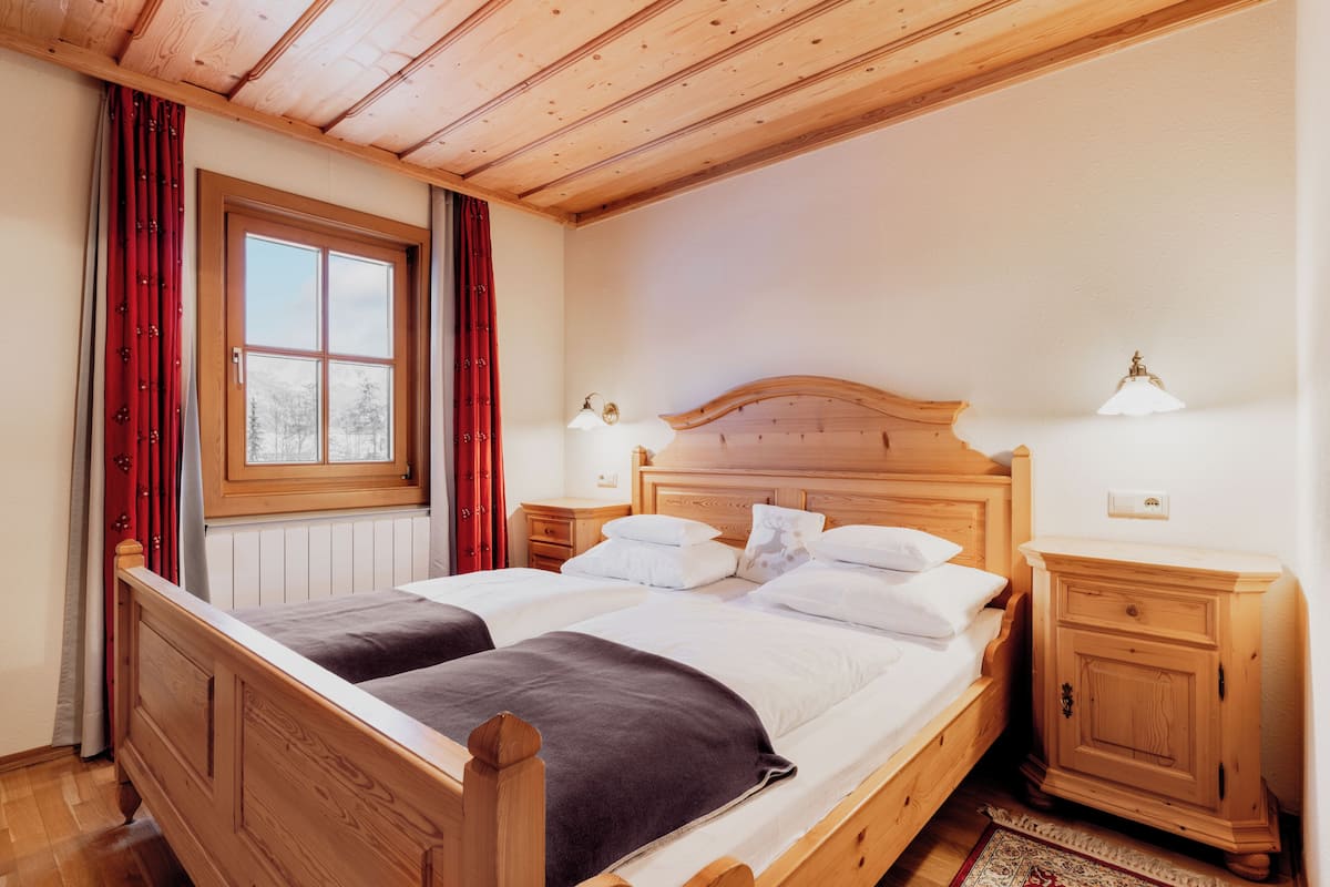 A wooden bed with two pillows and a nightstand with a lamp.