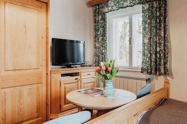 Un mueble de madera con un televisor, una mesa redonda con un florero y una ventana con cortinas florales.