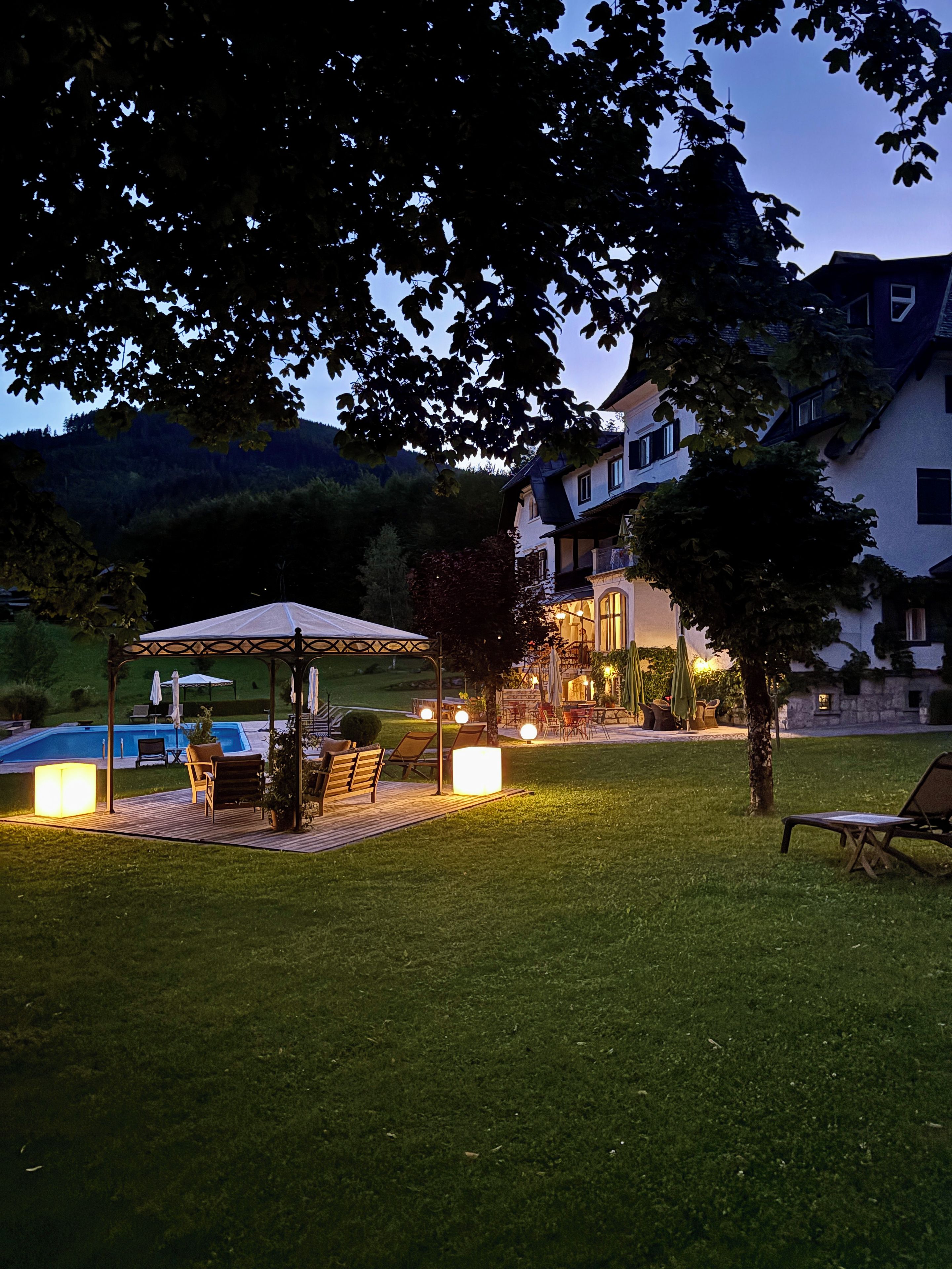A well-lit outdoor area with a pool, lounge chairs, and a covered seating area.