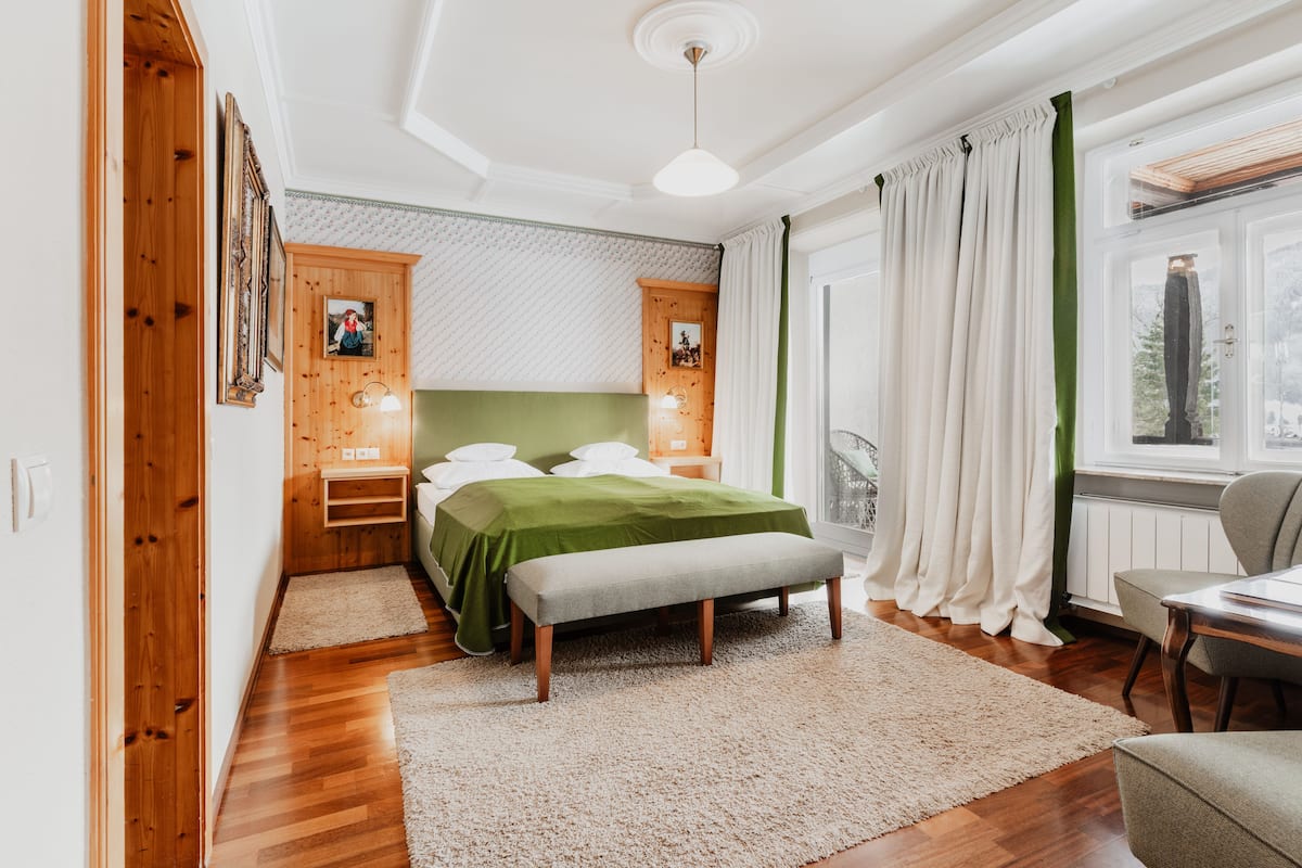 A bedroom with a bed, bedside tables, a bench, and a window with curtains.