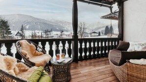 A balcony with wicker furniture, a table with a drink, and a view of a snowy mountain landscape. - Landhaus Koller (Gosau)