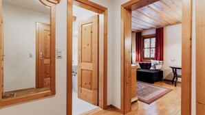 A hallway with wooden doors leading to a living area with a sofa and a window with red curtains. - Landhaus Koller (Gosau)