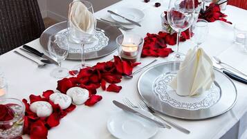 Una mesa dispuesta para una cena romántica, con pétalos de rosa, velas y cristalería elegante.
