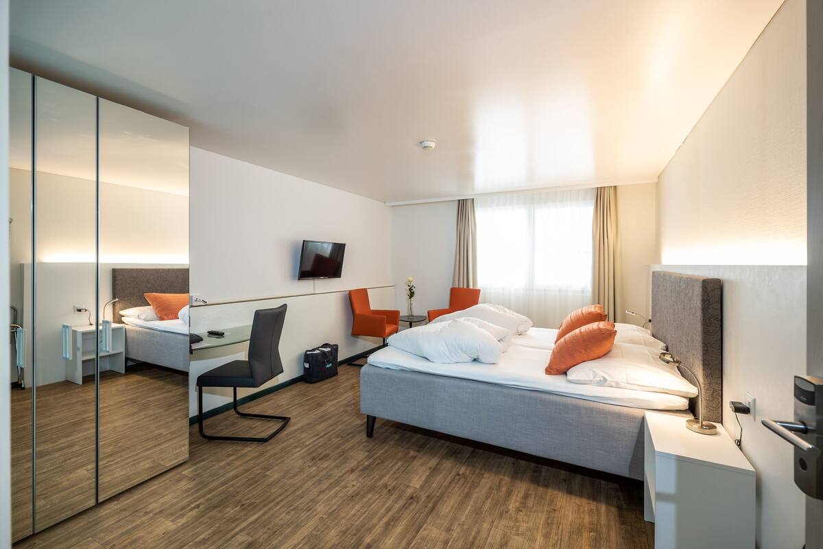 A modern hotel room with a bed, a desk, a chair, a TV, and a mirror.