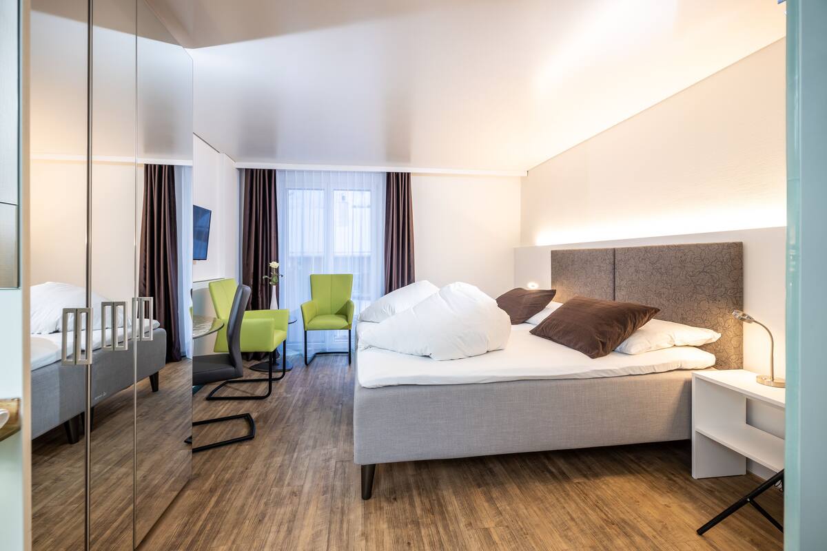A modern hotel room with a bed, a desk, a chair, and a mirror.