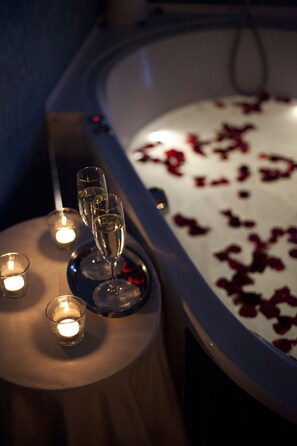 Eine Badewanne mit Rosenblüten, zwei Kerzen und drei Champagnergläsern auf einem kleinen Tisch.