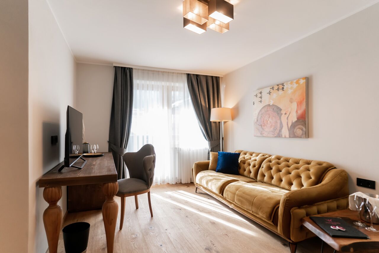 A modern living room with a wooden desk, a comfortable sofa, a television, and a painting on the wall.