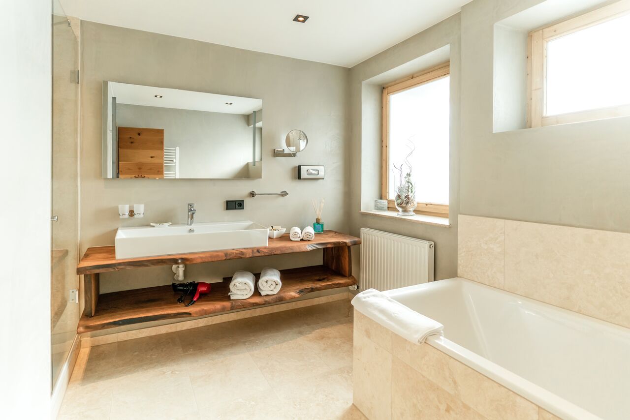A modern bathroom with a large bathtub, a wooden vanity with a sink, a mirror, and a window providing natural light.