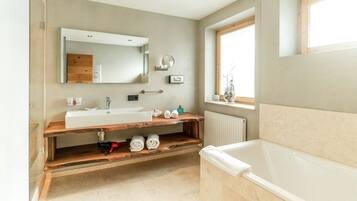 A modern bathroom with a large bathtub, a wooden vanity with a sink, a mirror, and a window providing natural light.