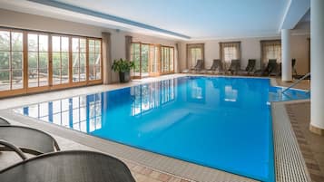 An indoor swimming pool with clear blue water, surrounded by windows and lounge chairs.