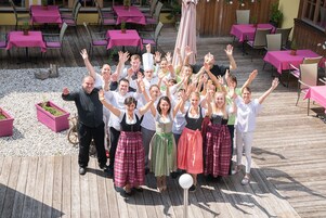 Un grupo de personas al aire libre en una terraza de madera con mesas y sillas, algunas vestidas con atuendo tradicional.