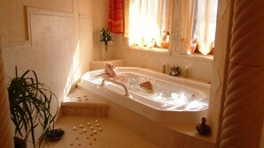 A bathroom with a bathtub, a window with curtains, a potted plant, and candles. - Alpen Adria Hotel & Spa (Hermagor-Pressegger See)