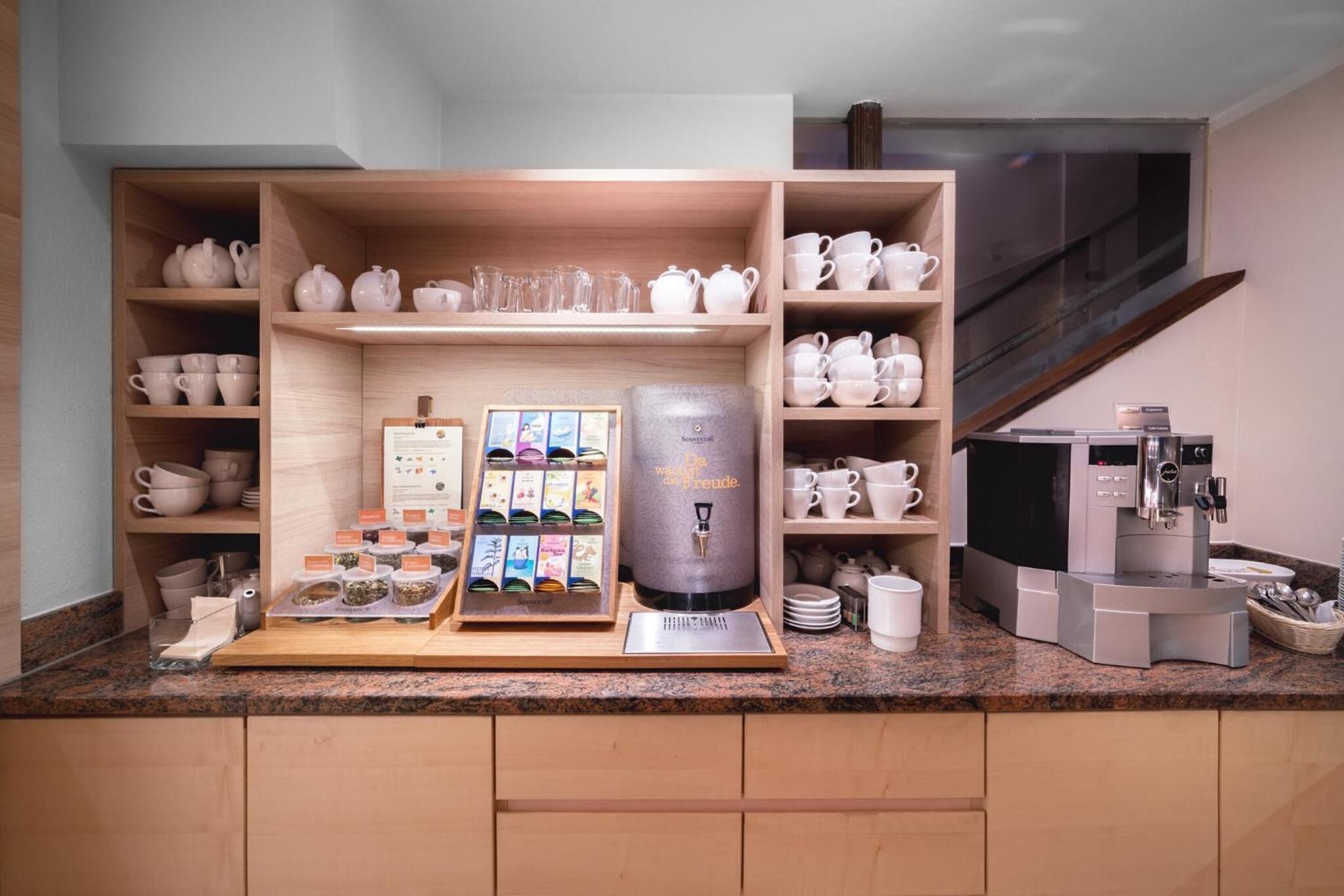 Una estación de café con cafetera, tetera y diferentes tazas y vasos.