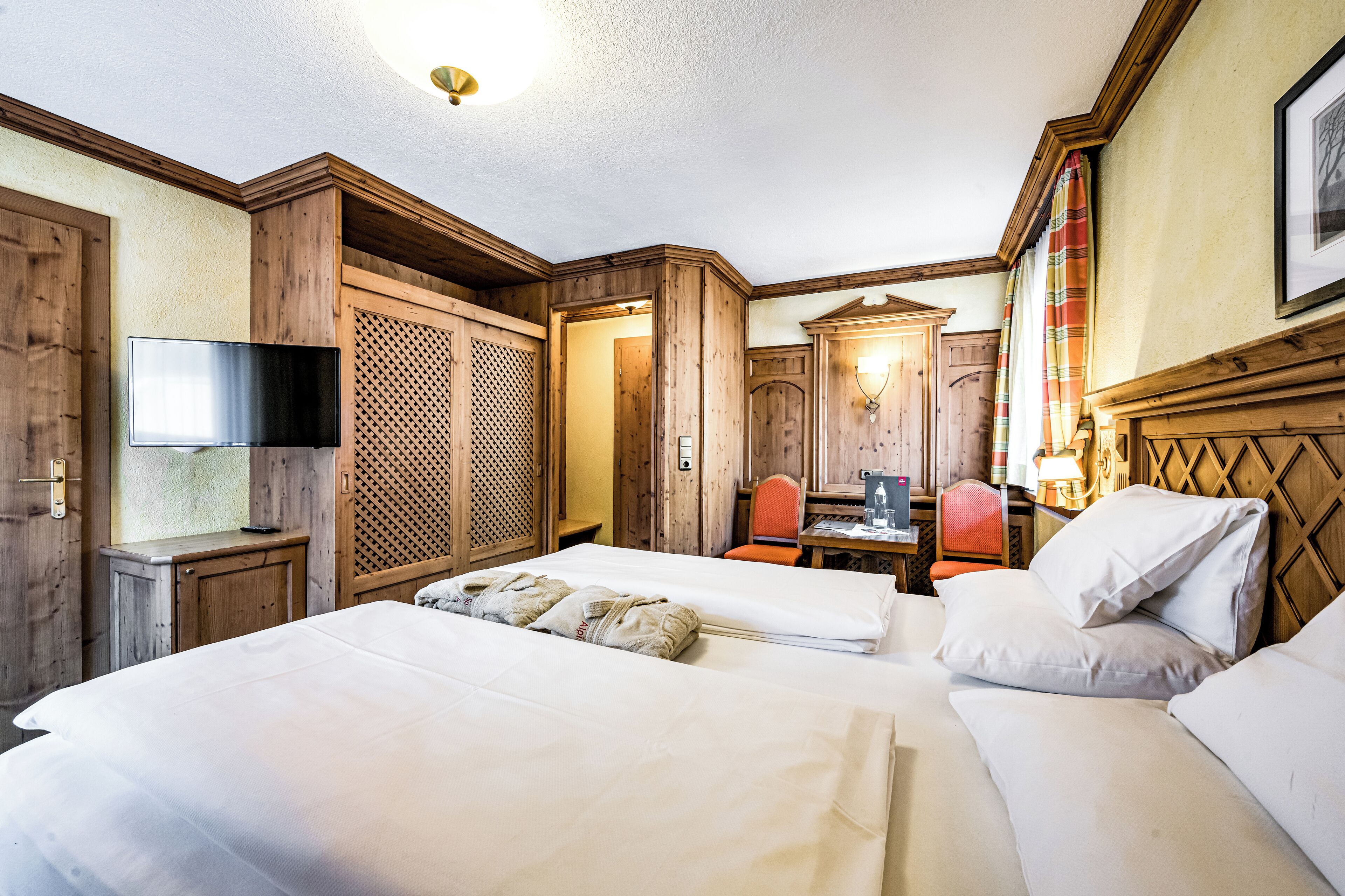 A hotel room with two beds, a TV, a desk with a chair, and wooden paneling.