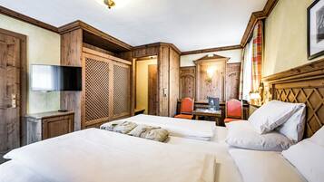 A hotel room with two beds, a TV, a desk with a chair, and wooden paneling.