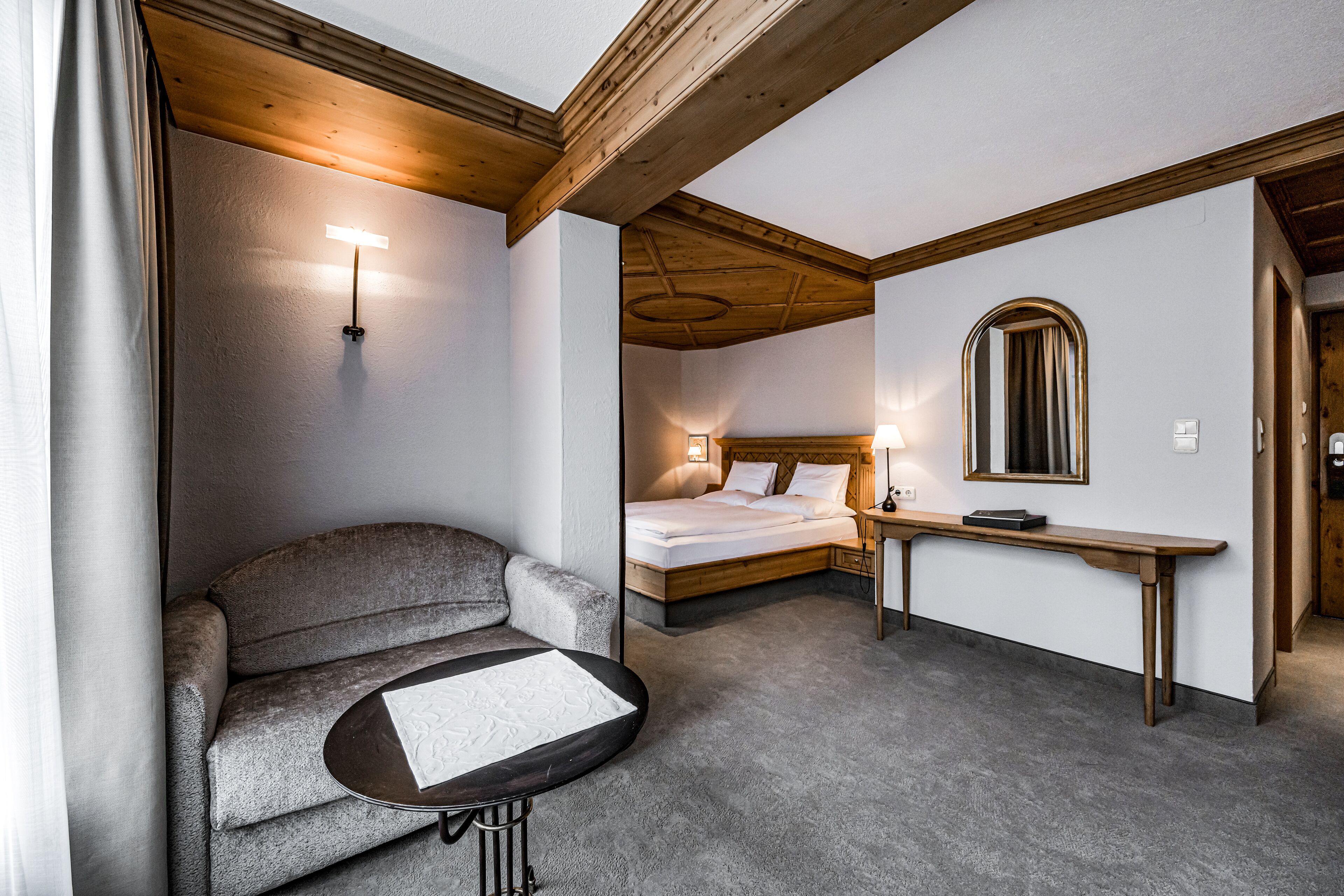 Una camera d'albergo con un divano, un tavolino, un letto, un comodino e uno specchio.