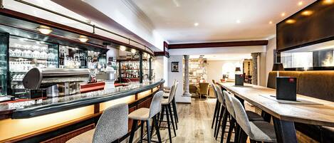 A bar area with stools, a counter with glasses and bottles, and a wooden table with chairs.