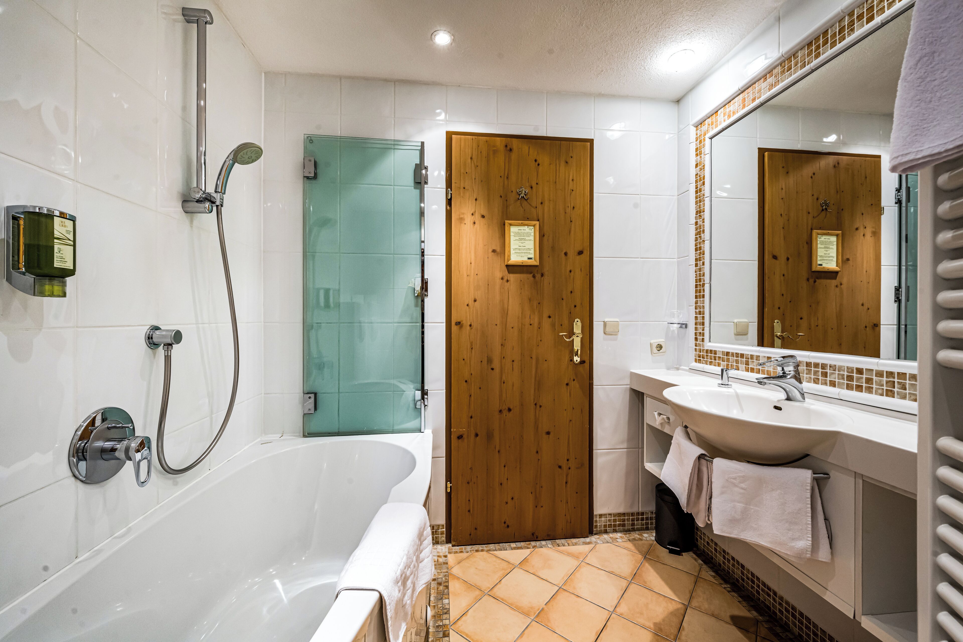 Une salle de bain avec une baignoire, une porte en bois, un espace de douche en verre et un lavabo avec un miroir.