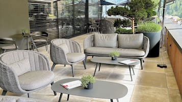 A covered outdoor seating area with wicker furniture, a table, and a potted plant.