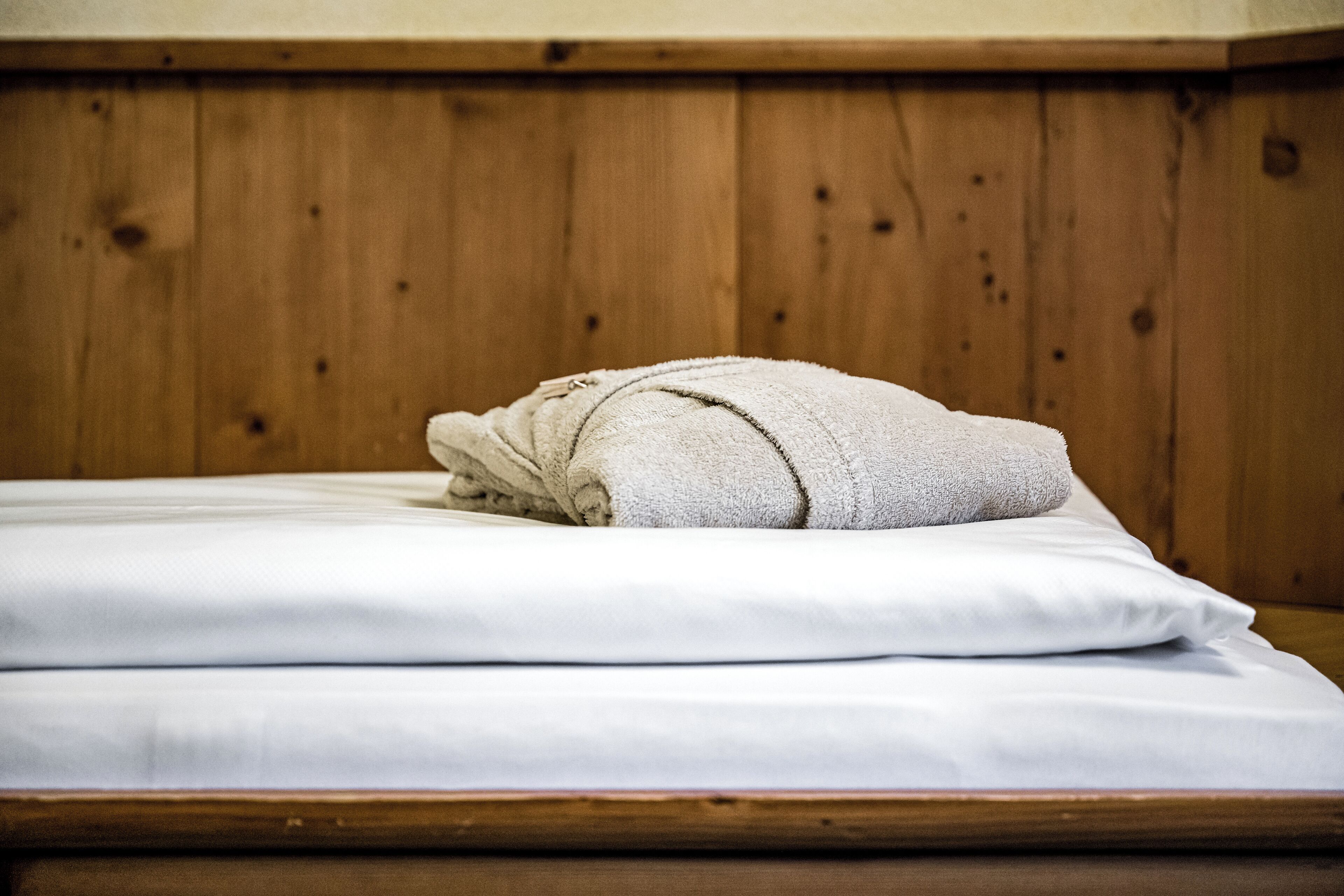 Un lit bien fait, avec des draps blancs et une serviette enroulée posée sur le dessus, le tout mis en valeur par une tête de lit en bois.