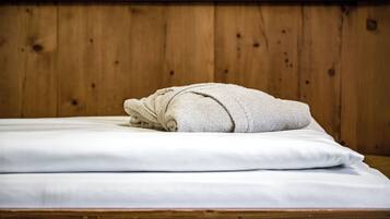 Un lit bien fait, avec des draps blancs et une serviette enroulée posée sur le dessus, le tout mis en valeur par une tête de lit en bois.