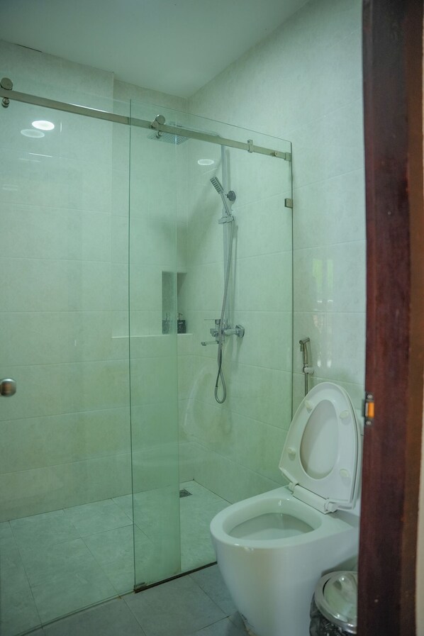 A bathroom with a glass-enclosed shower, a white toilet, and a trash bin. - Villa Oasis Luang Prabang (Luang Prabang)