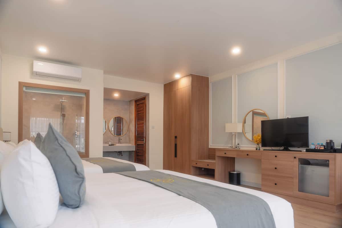 A modern hotel room with a large bed, a desk with a TV, a mirror, and a bathroom with a shower and toilet.