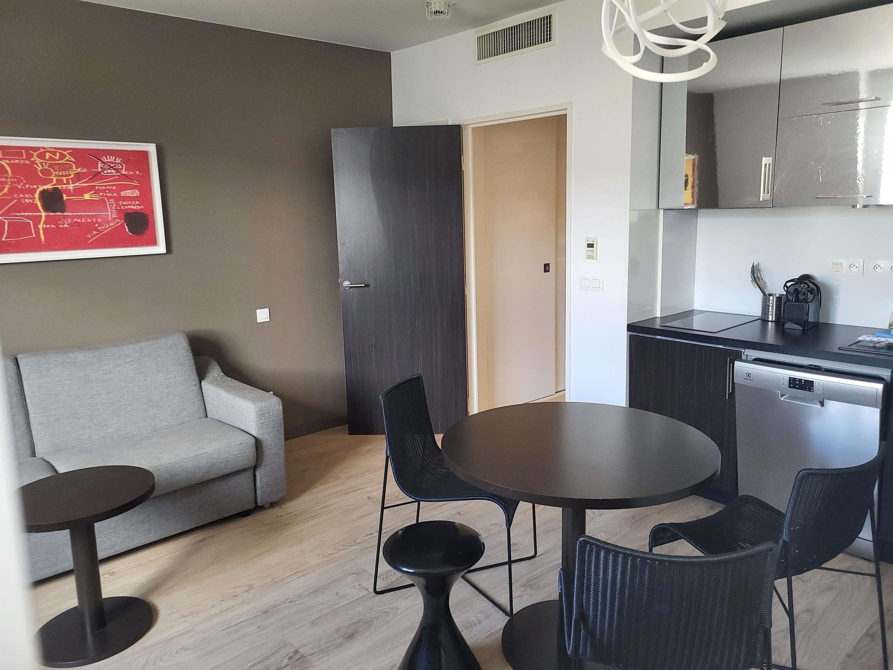 Un salon moderne avec un canapé gris, une table de salle à manger ronde et des chaises noires.