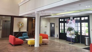 A lobby with a modern design, featuring a reception desk, colorful seating, and a large window.