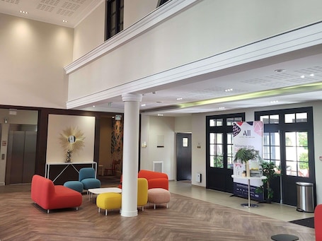 A lobby with a modern design, featuring a reception desk, colorful seating, and a large window.. Aparthotel Adagio Serris - Val d'Europe