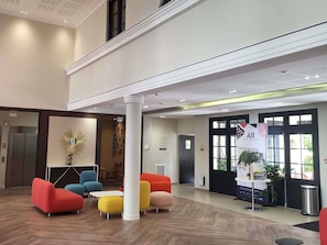 A lobby with a modern design, featuring a reception desk, colorful seating, and a large window. - Aparthotel Adagio Serris - Val d'Europe (Serris)