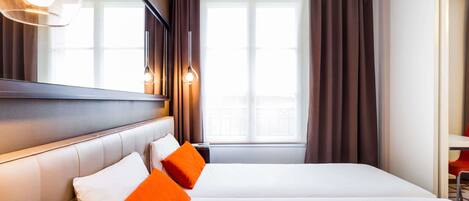 Une chambre d’hôtel avec un grand lit, deux oreillers, une table de chevet, un miroir et une fenêtre avec des rideaux.
