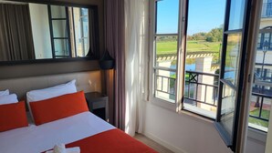 A hotel room with a large bed, a nightstand, a mirror, and a window with a view of a green landscape.