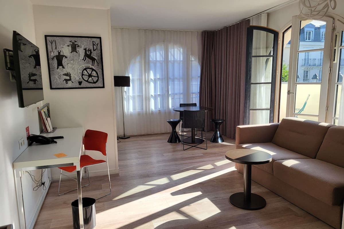 Ein modernes Wohnzimmer mit einer Couch, einem Esstisch mit Stühlen, einem kleinen Beistelltisch und einem an der Wand befestigten Fernseher.