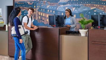 En receptionsdisk med en väggmålning som föreställer en stadsbild, en receptionist och två gäster.