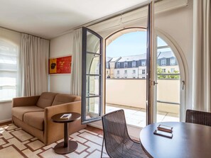 Een kamer met een bank, een kleine tafel, een rieten stoel en een grote glazen deur die leidt naar een buitenruimte.