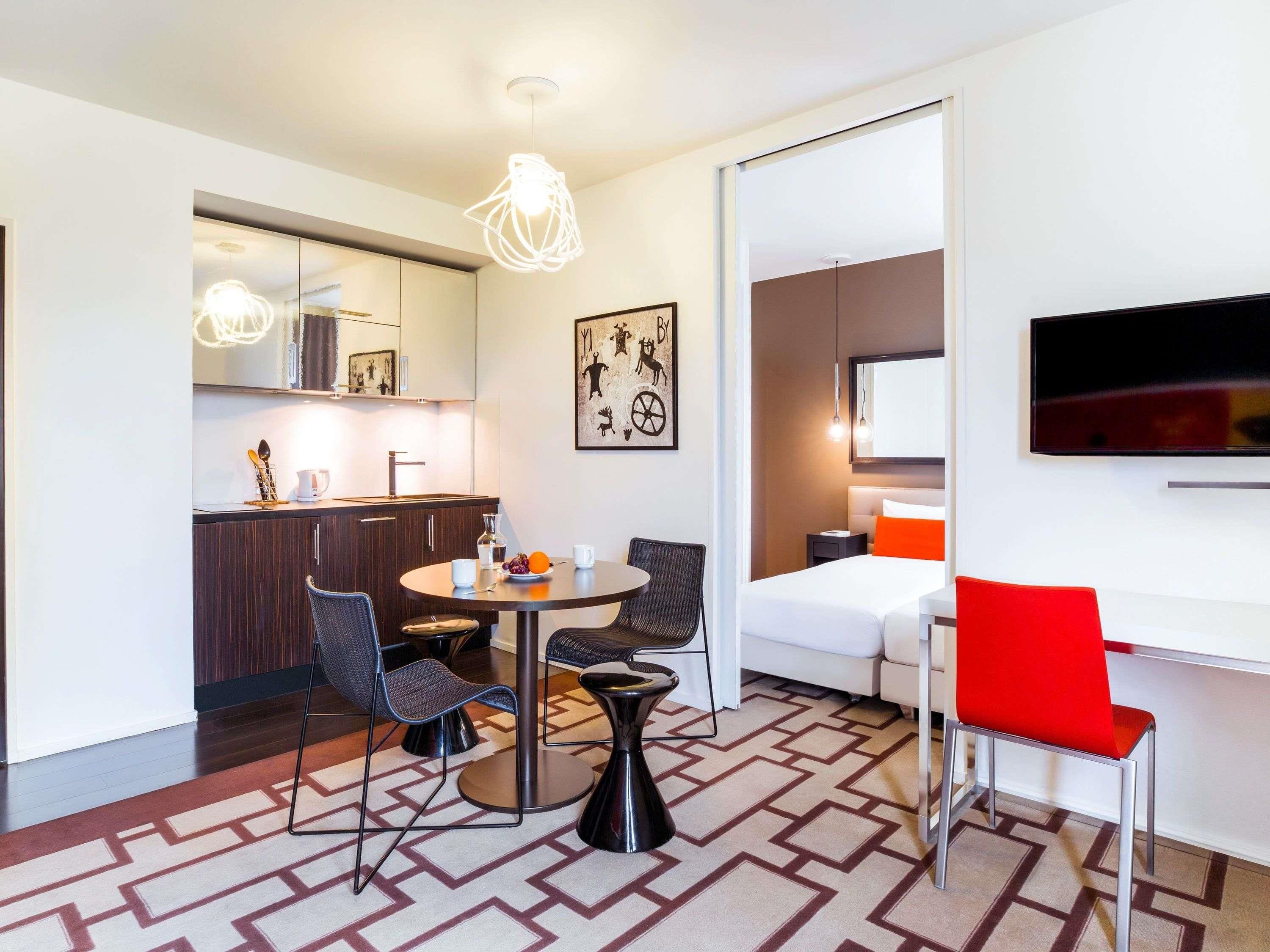 Ein modernes Hotelzimmer mit Essbereich, Küchenzeile und einem Bett mit Fernseher.