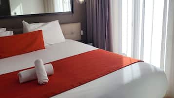 Une chambre d’hôtel avec un lit, du linge de lit blanc, un plaid rouge et une serviette enroulée.