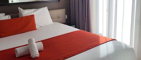 Una habitació d'hotel amb un llit, roba de llit blanca, una manta vermella i una tovallola arremolinada.