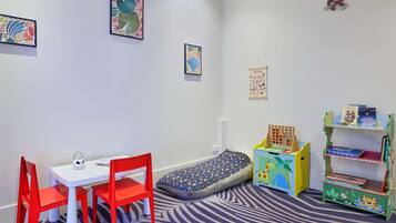 Ein Kinderzimmer mit Bett, Schreibtisch, Stühlen, einem Bücherregal und Wanddekorationen.