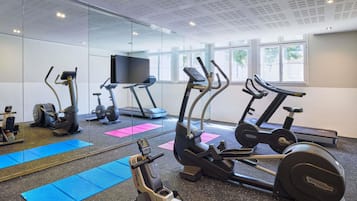 A gym with exercise equipment, a large mirror, and windows.