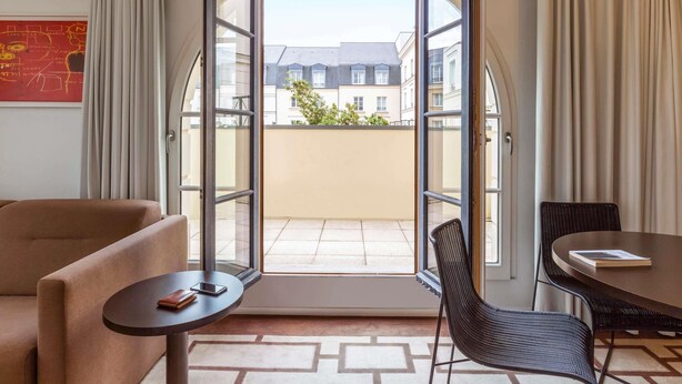 A hotel room with a large arched window, a sofa, a small table, a chair, and a dining table.