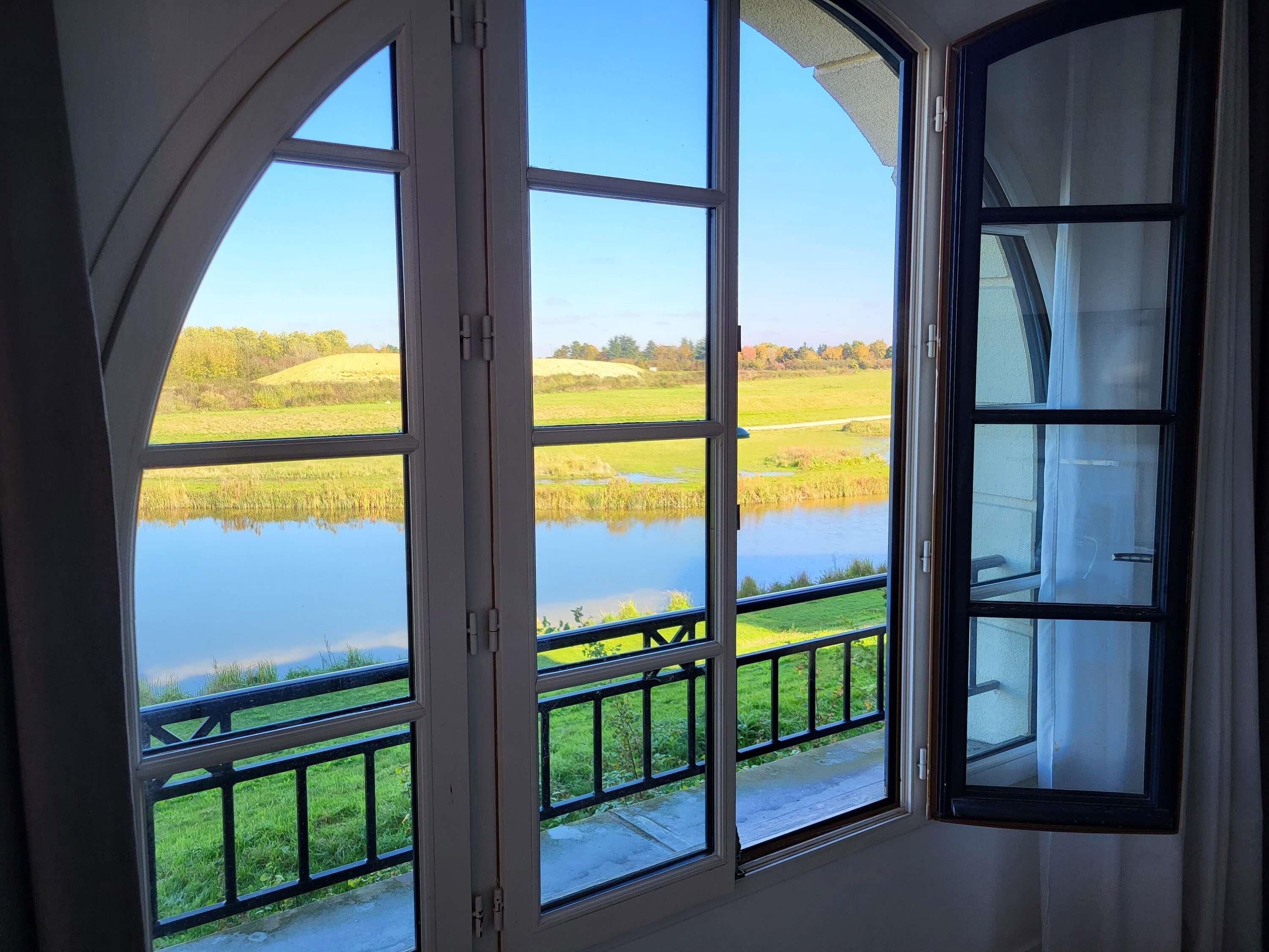 A room with a large arched window overlooking a pond and grassy fields.