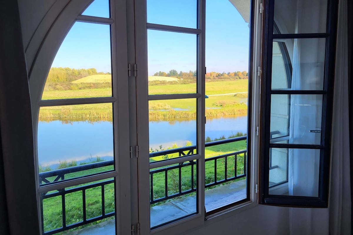 Ein Zimmer mit einem großen Bogenfenster mit Blick auf einen Teich und Wiesen.