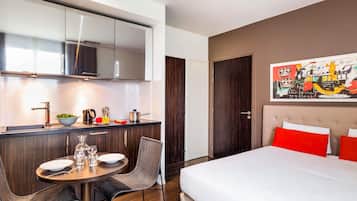 Une chambre d’hôtel moderne dotée d’une kitchenette, d’un coin repas et d’un grand lit avec des oreillers rouges.