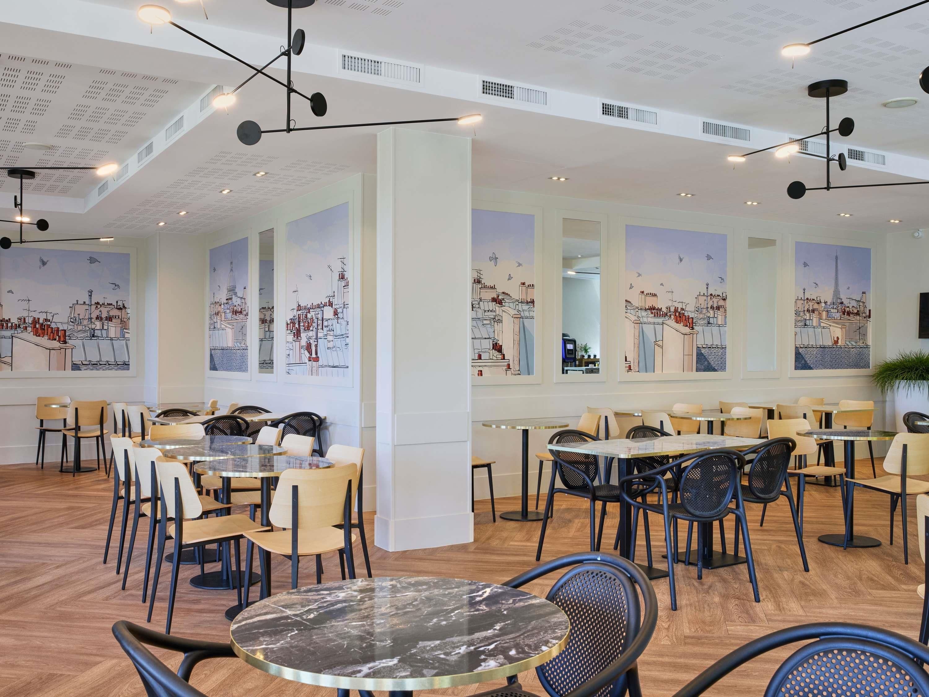 A modern dining area with high ceilings, pendant lighting, and cityscape murals on the walls.