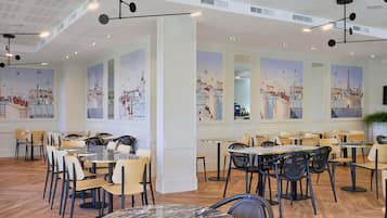 A modern dining area with high ceilings, pendant lighting, and cityscape murals on the walls.